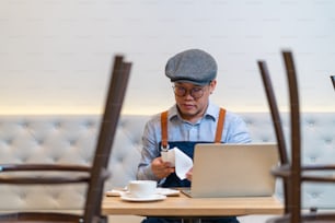 Asian man coffee shop owner sitting at table and calculating shop finance bill on laptop computer after closed. Stressed male small business restaurant entrepreneur counting payment and income bills.