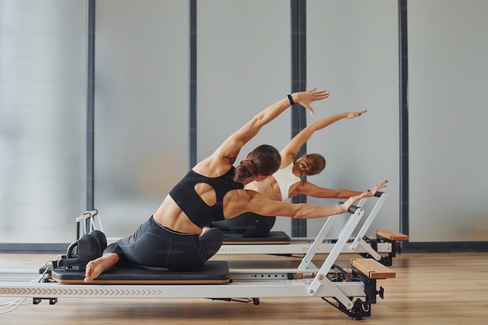 Uso de equipos de gimnasio. Dos mujeres con ropa deportiva y cuerpos delgados tienen un día de fitness yoga juntas en el interior.