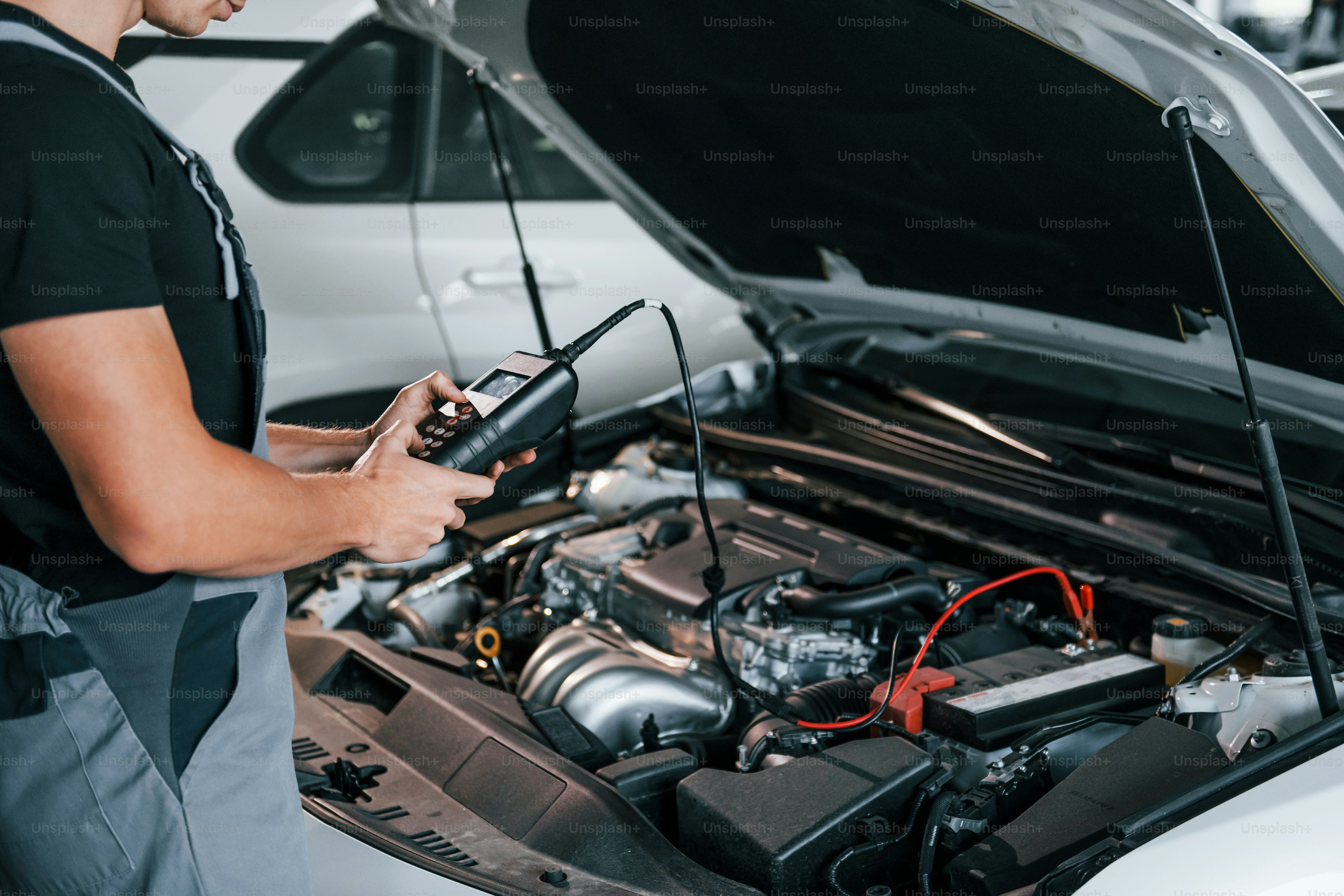 Special tool for testing characteristics. Adult man in grey colored uniform works in the automobile salon.
