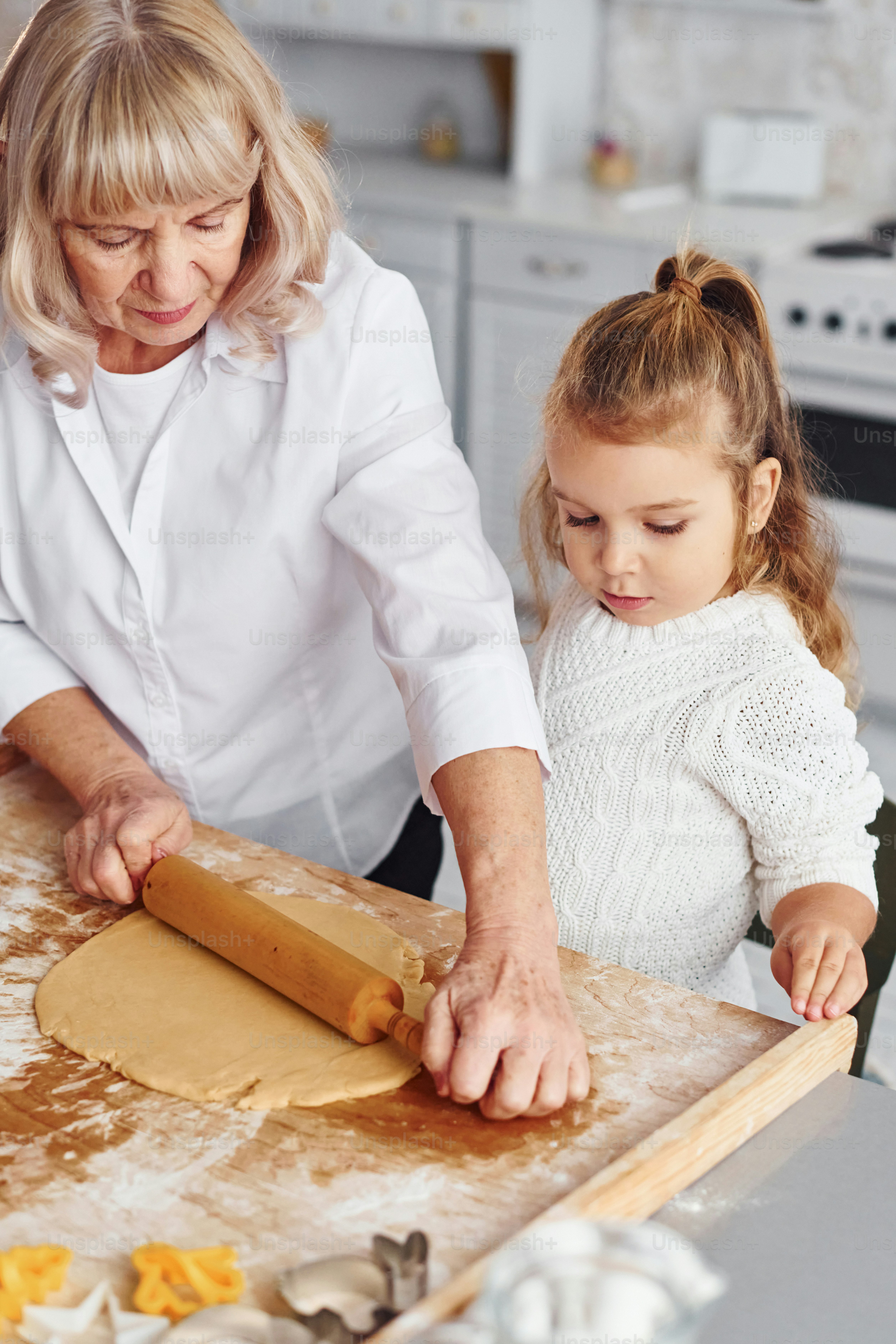 Senior grandmother with her little granddaughter cooks sweets for Christmas on the kitchen.