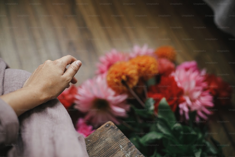 Donna mano sul vestito di lino sullo sfondo del bouquet di fiori autunnali sul pavimento, mano da vicino. Vita lenta. Fioraio che dispone bellissime dalie colorate. Stagione autunnale in campagna