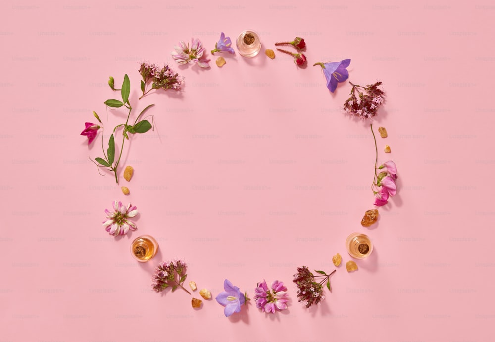 에센셜 오일 병, 유향, 장미 및 원형 복사 공간이 있는 다양한 여름 꽃이 있는 분홍색 파스텔 배경