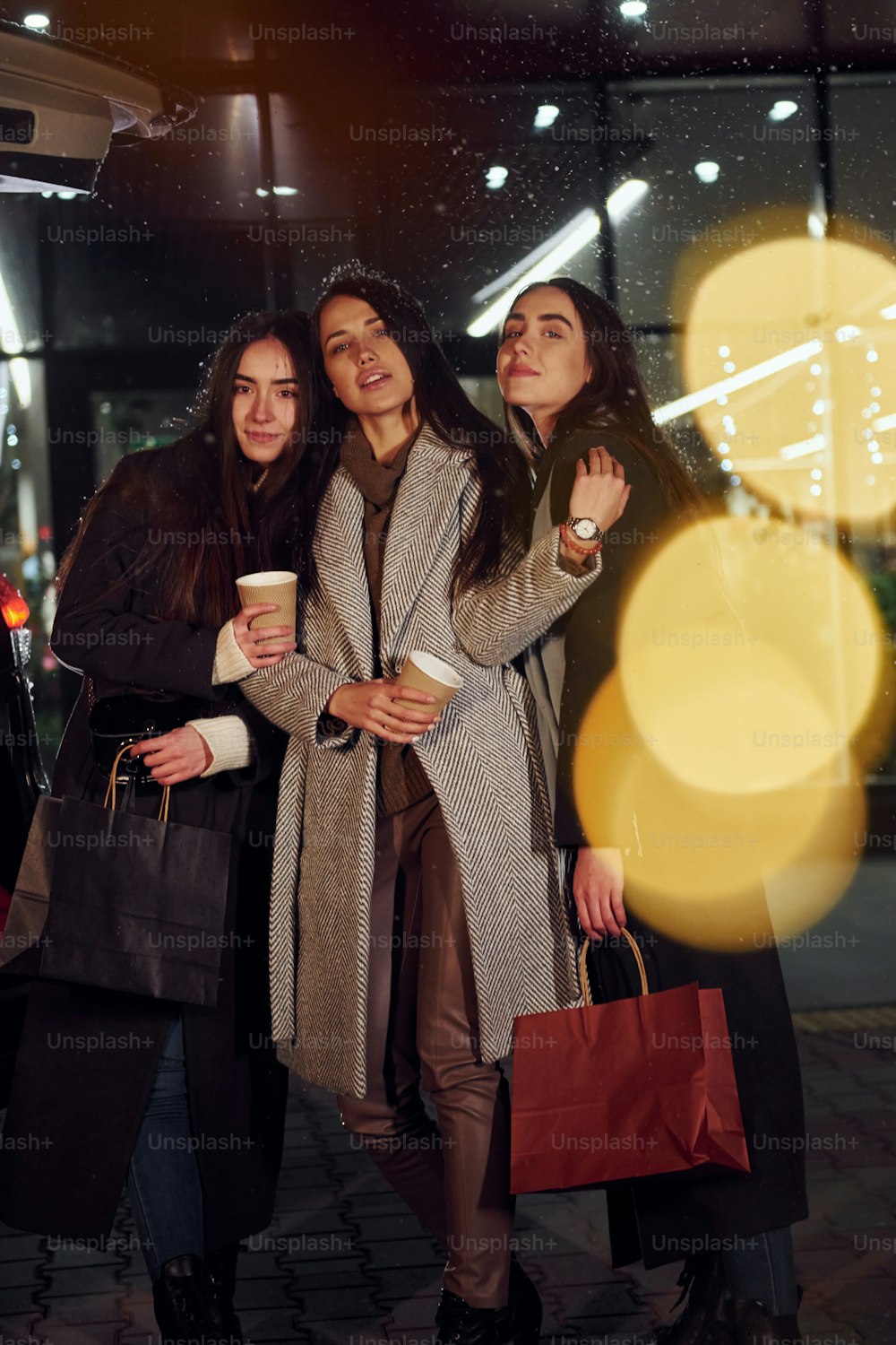 Copos de bebida nas mãos. Três mulheres alegres passam as férias de Natal juntas ao ar livre. Concepção de ano novo.