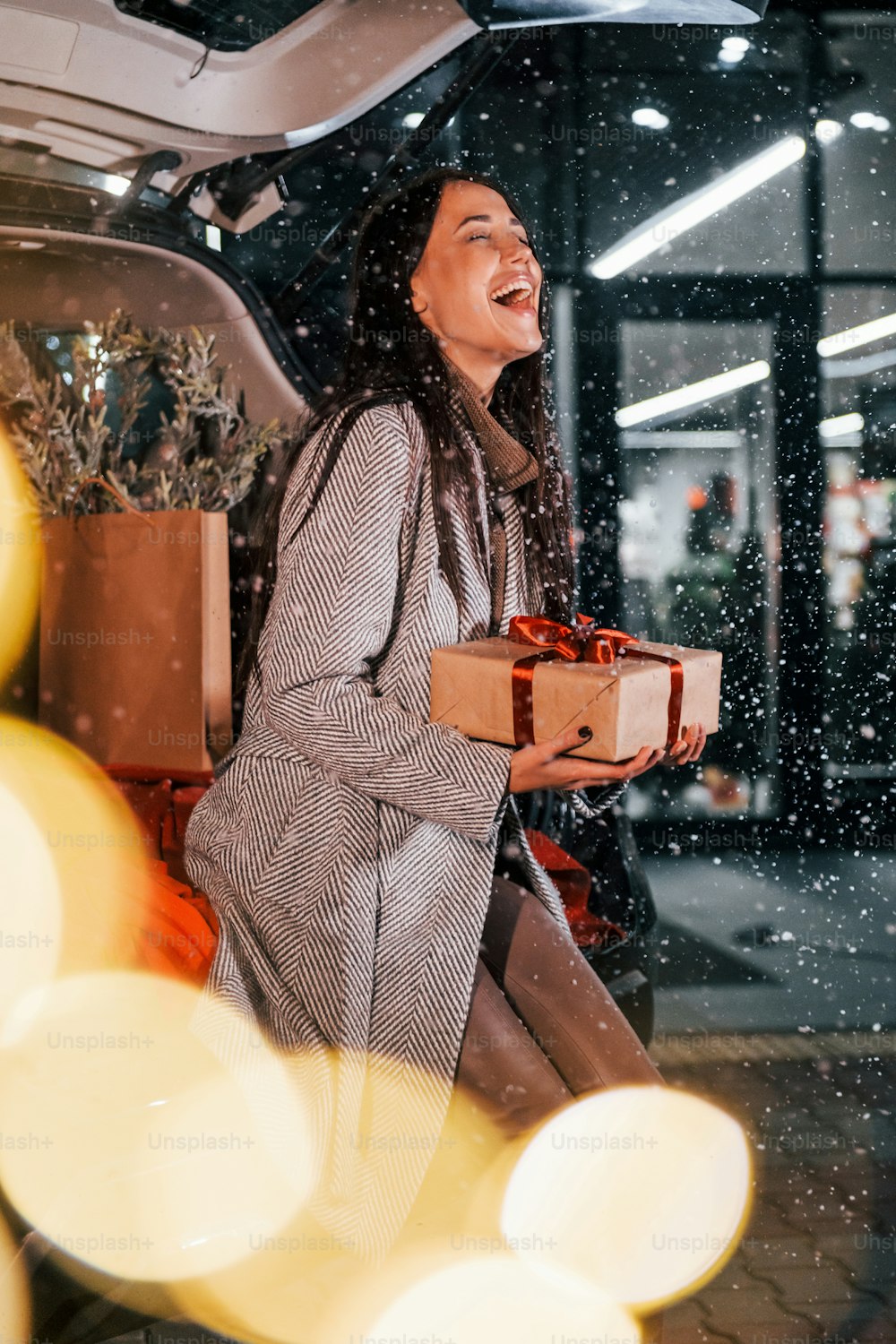 Near the car with gift box. Cheerful woman is outdoors at Christmas holidays time. Conception of new year.