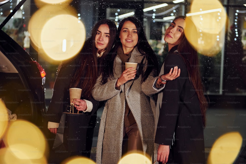 Cups of drink in hands. Three cheerful women spends Christmas holidays together outdoors. Conception of new year.