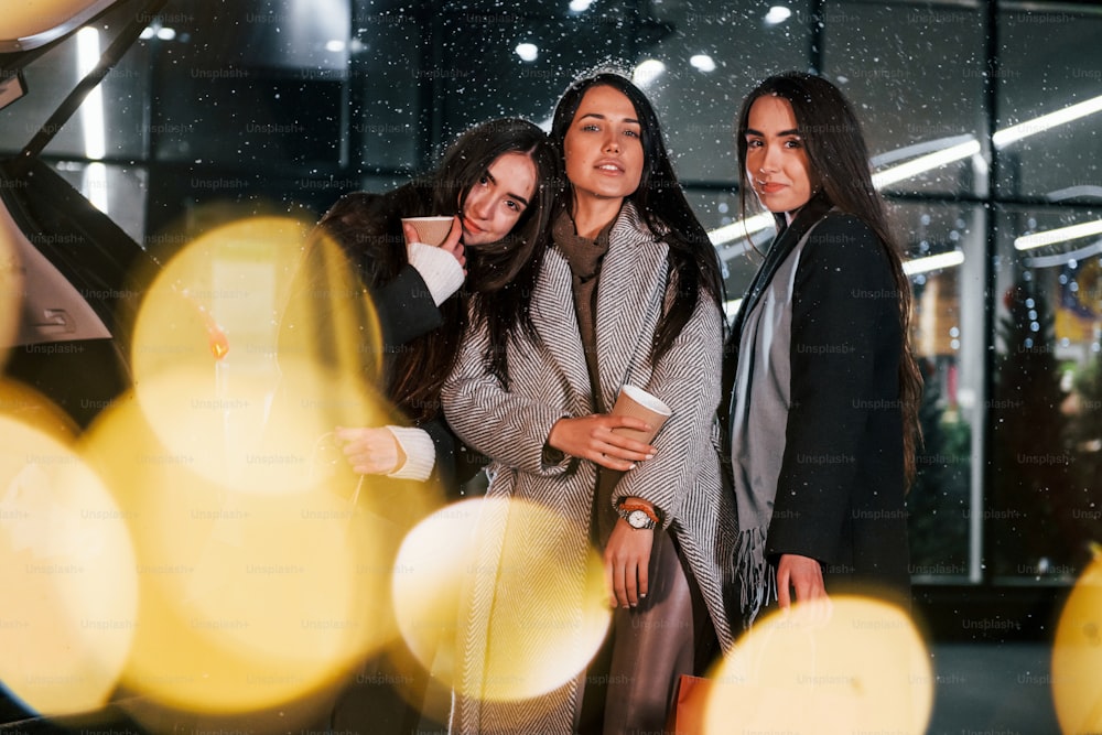 Vasos de bebida en las manos. Tres alegres mujeres pasan juntas las fiestas navideñas al aire libre. Concepción del año nuevo.