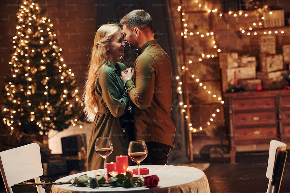 De pé na sala decorada de Natal. Jovem casal adorável tem jantar romântico dentro de casa juntos.