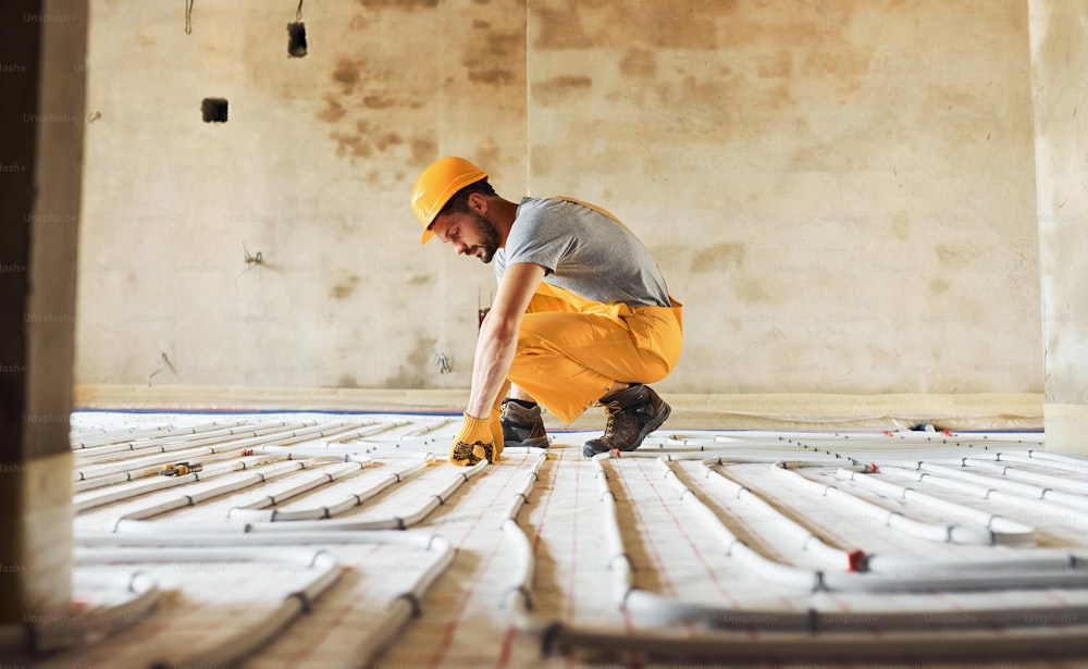 Worker in yellow colored uniform installing underfloor heating system.