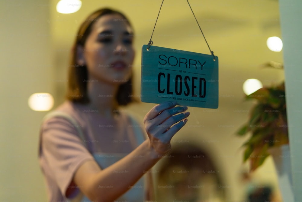 Asian woman coffee shop barista walking to cafe door and turning hanging closed sign. Female waitress preparing restaurant for service to customer. Small business owner and part time job working concept