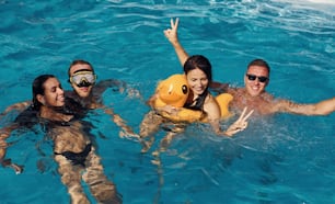 Using yellow colored duck to swim. Group of young happy people have fun in swimming pool at daytime.