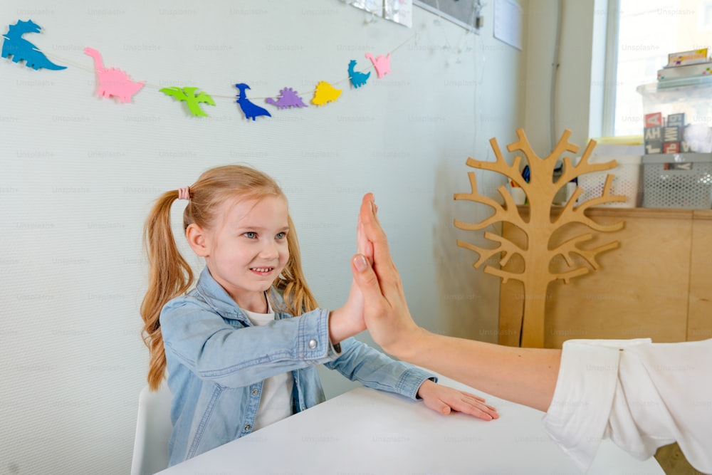 Happy little 5 years girl giving high five to her teacher after good work at lesson or session in kindergarten.