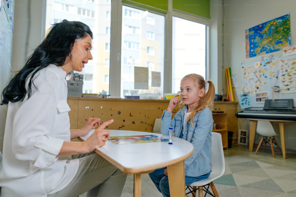Girl on the session of speech therapist. Lesson on the development of speech in kindergarten. Teacher spreads out puzzle in front of the child.