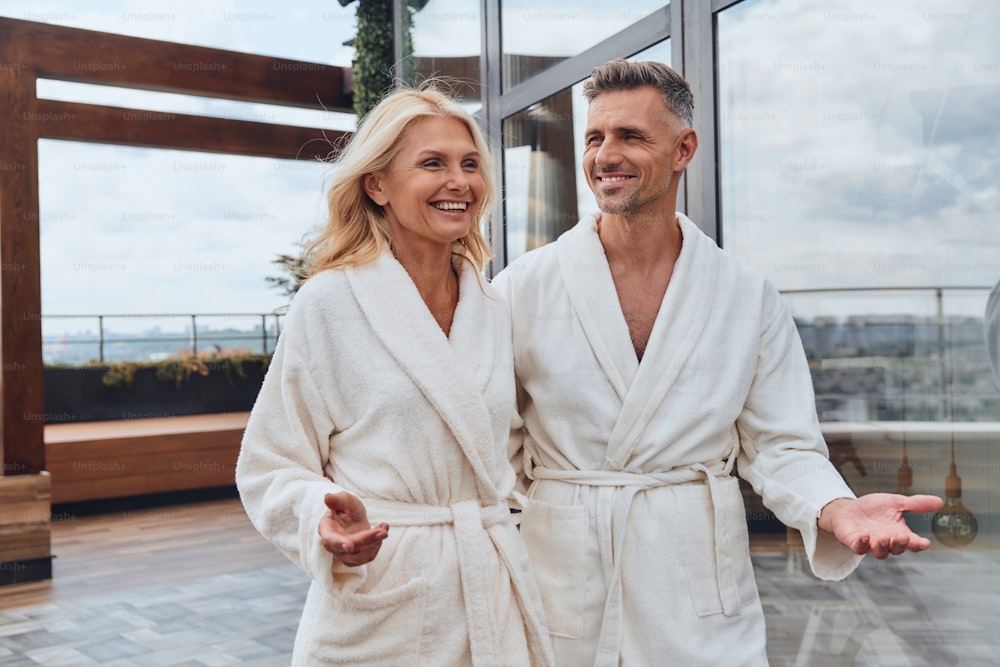 Beautiful mature couple in bathrobes enjoying fruits and wine while relaxing in luxury hotel outdoors