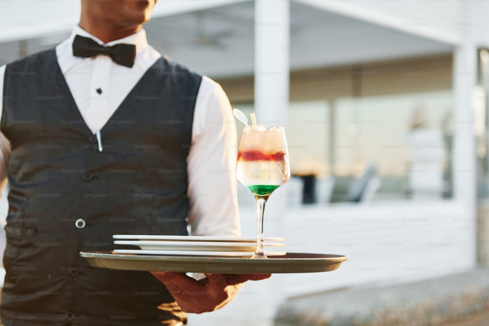 Close up view of drink. Black waiter in formal clothes is at his work outdoors at sunny daytime.