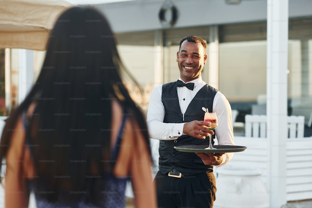 Orden para la mujer. Un camarero negro vestido de gala está en su trabajo al aire libre durante el día soleado.