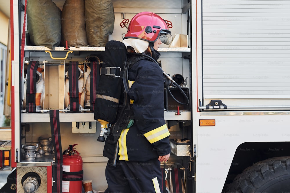 Nimmt Ausrüstung. Feuerwehrfrau in Schutzuniform in der Nähe des Lastwagens.
