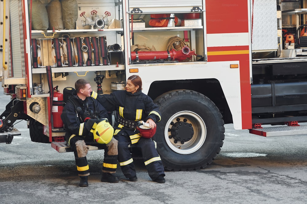 Male and female firefighters in protective uniform is outdoors together.