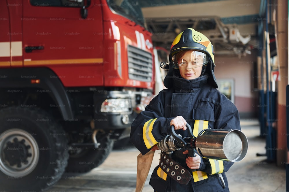 Hose in hands. Female firefighter in protective uniform standing near truck.