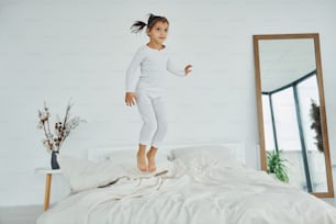Active little girl jumps on the bed. Interior and design of beautiful modern bedroom at daytime.