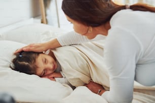 Little girl sleeps and mom looked and her. Interior and design of beautiful modern bedroom at daytime.