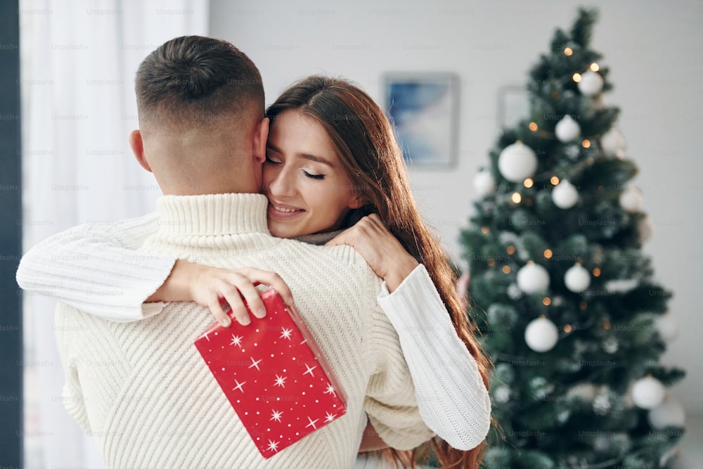 Girls holds red gift box. Young romantic couple celebrates New year together indoors.