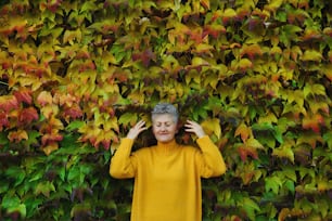 色とりどりの自然の秋の背景に屋外に立って、目を閉じた年配の女性の肖像画。