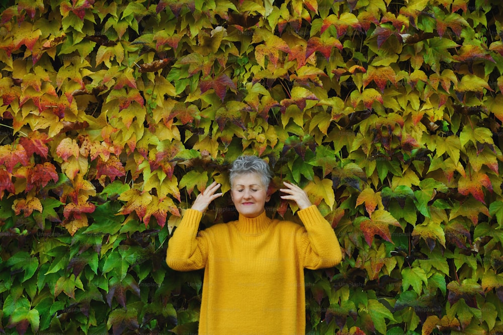 Portrait of senior woman standing outdoors against colorful natural autumn background, eyes closed.