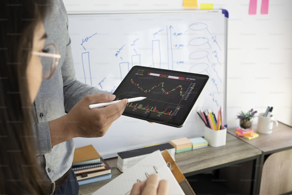 オフィスでデジタルタブレットでグラフの株式市場データを一緒に分析するビジネスパーソン。