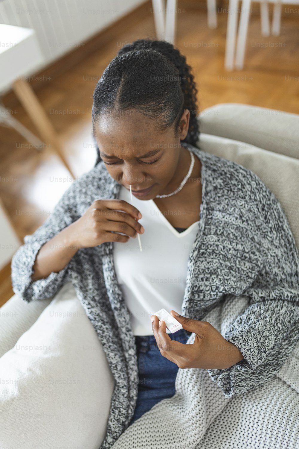 African-American woman using cotton swab while doing coronavirus PCR test at home. Woman using coronavirus rapid diagnostic test. Young woman at home using a nasal swab for COVID-19.