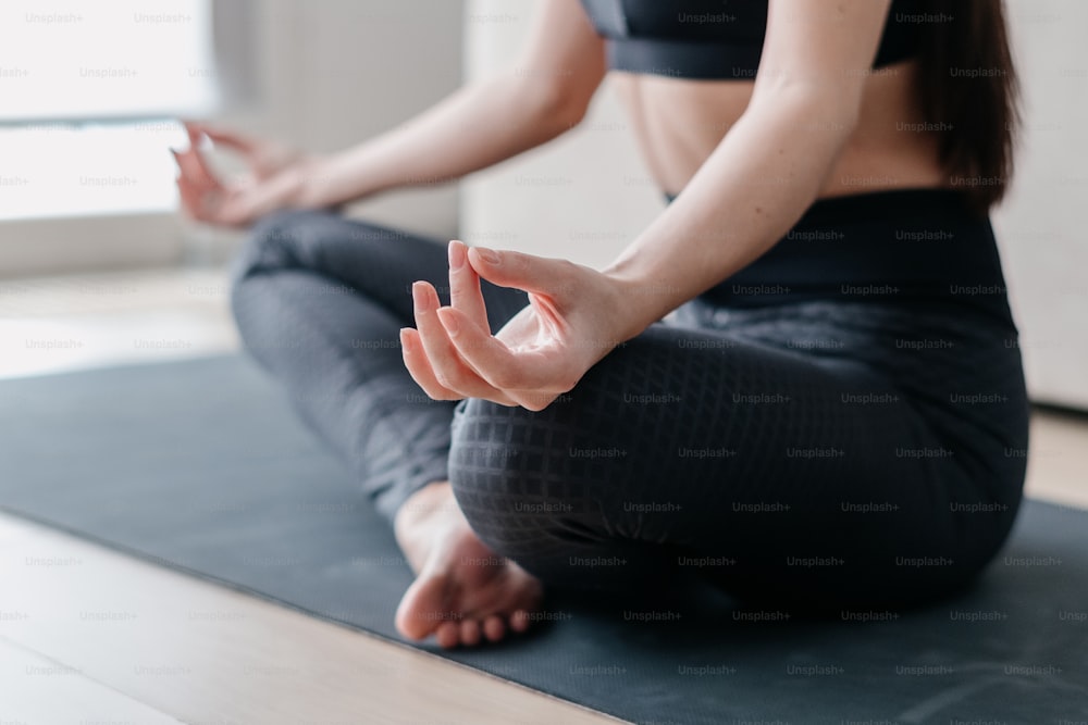 Cropped shot of sporty woman in sports clothes keeping hands in mudra gesture, meditating to feel calm relief stress during yoga training and meditation at home, Life balance and mindfulness concept