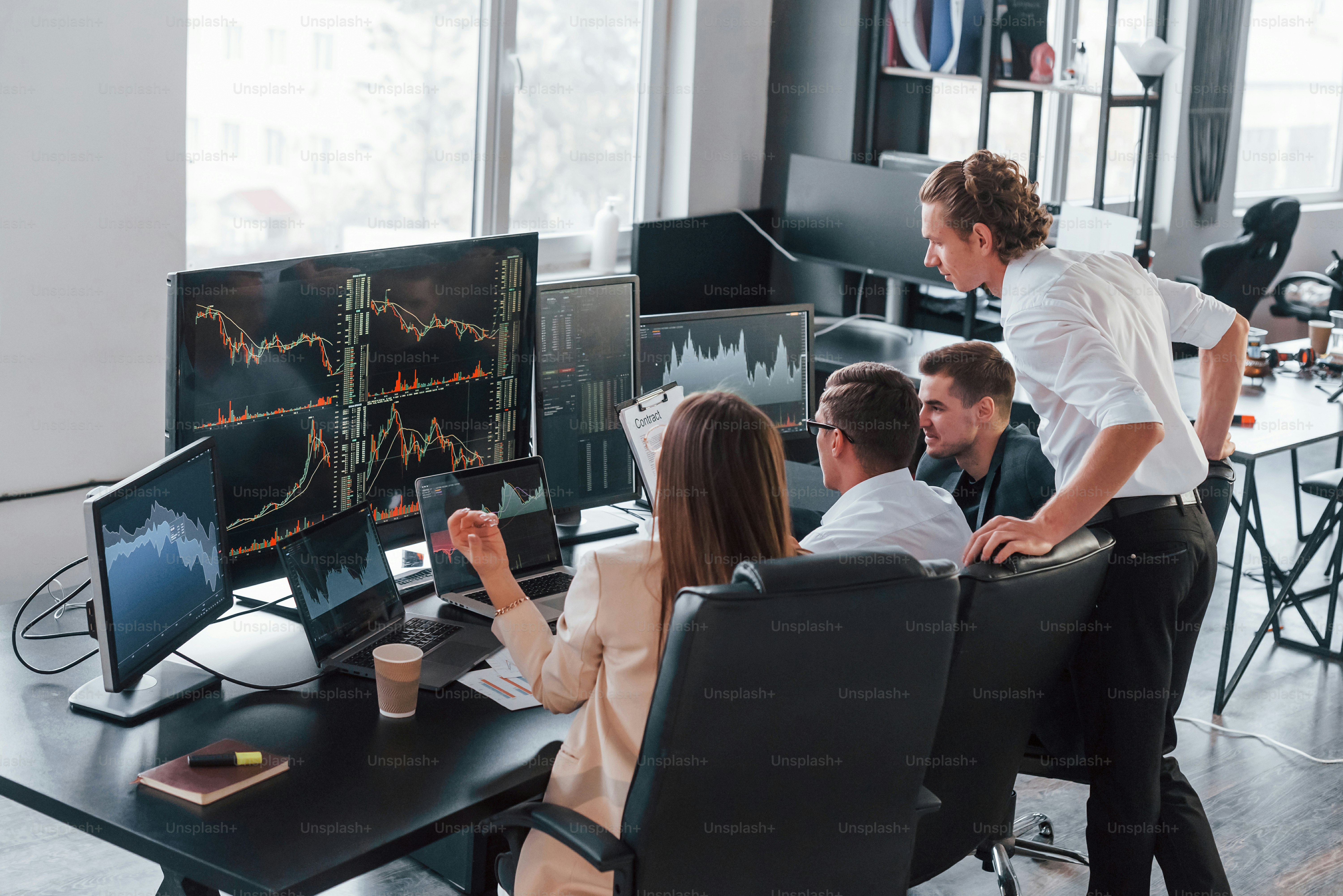 Holds document in hands. Team of stockbrokers works in modern office with many display screens.