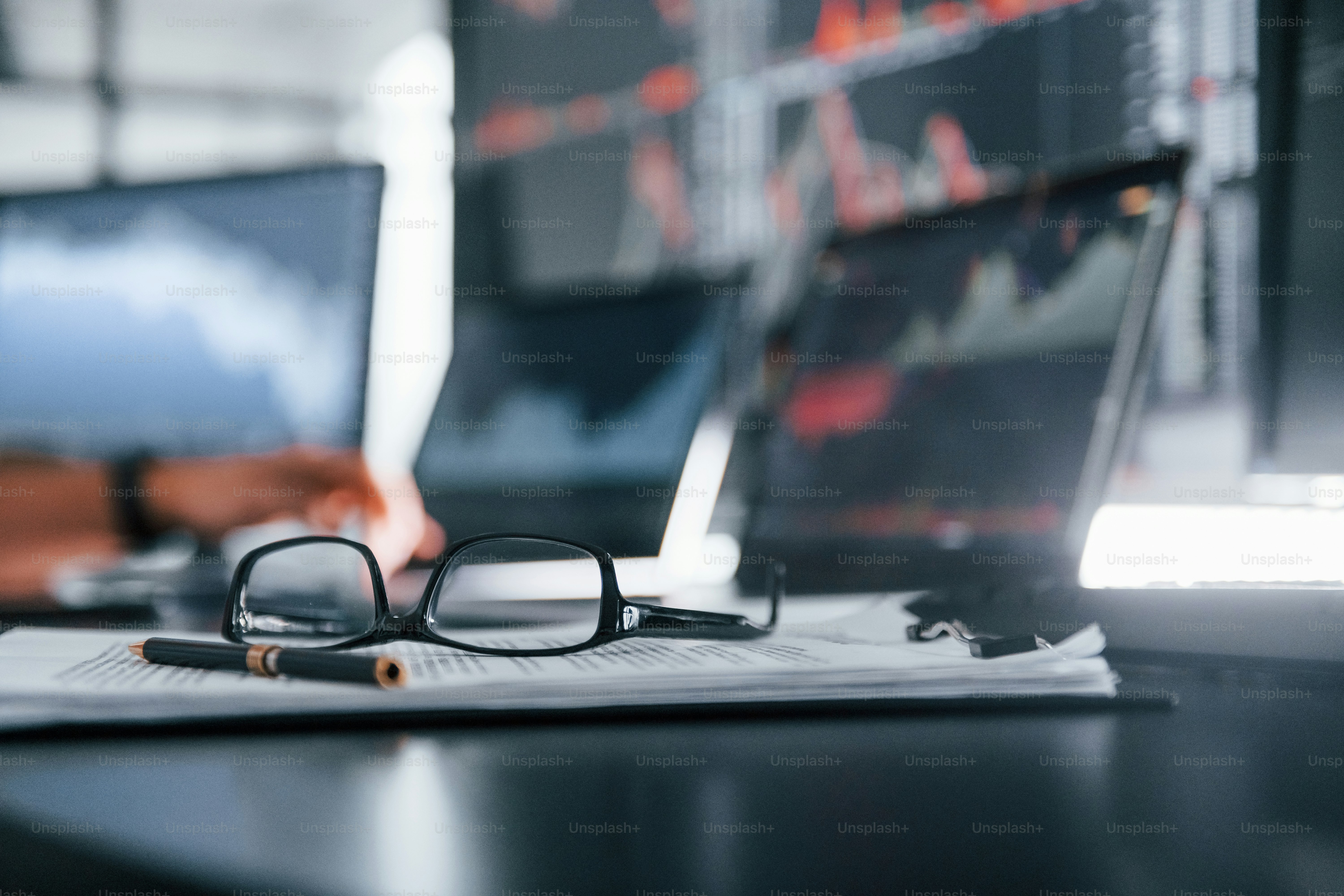 Close up focused view of glasses, notepad, documents and man at background.