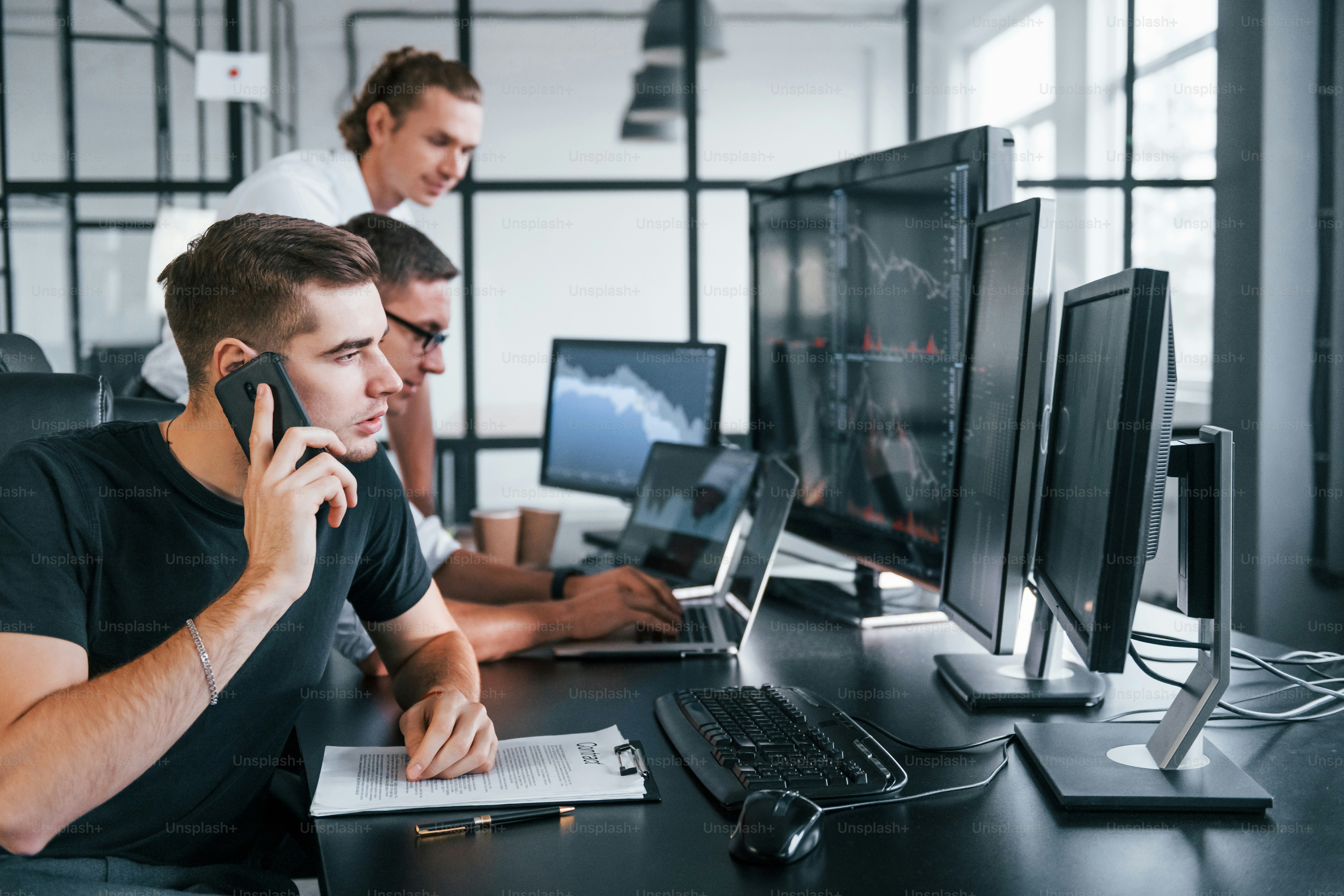 Guy talks by phone. Team of stockbrokers works in modern office with many display screens.