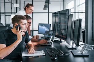 Guy talks by phone. Team of stockbrokers works in modern office with many display screens.