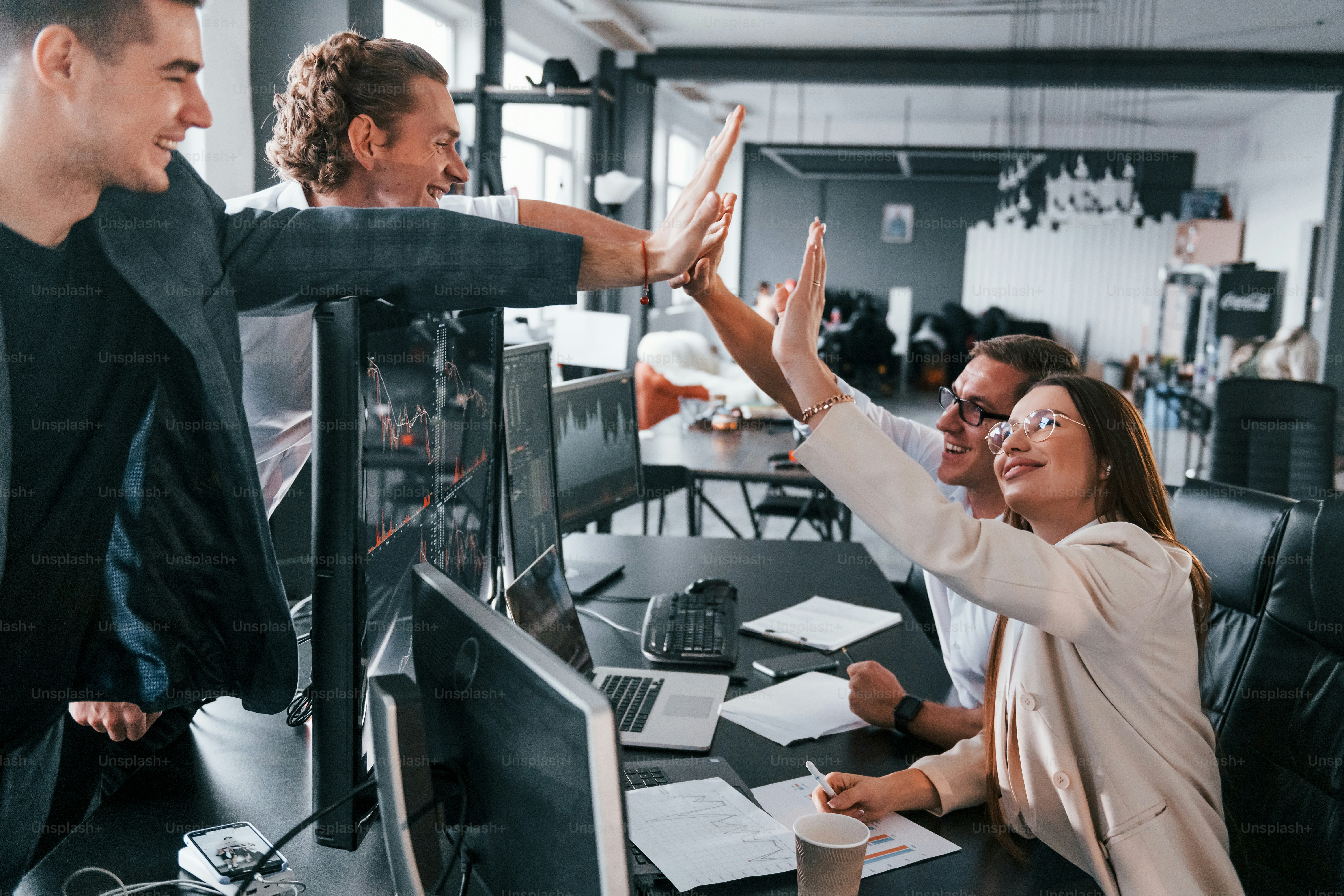 Giving high five. Team of stockbrokers works in modern office with many display screens.