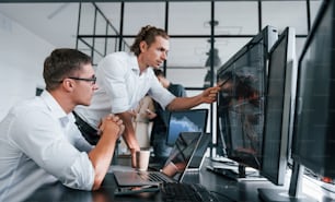 Sitting by the table. Team of stockbrokers works in modern office with many display screens.