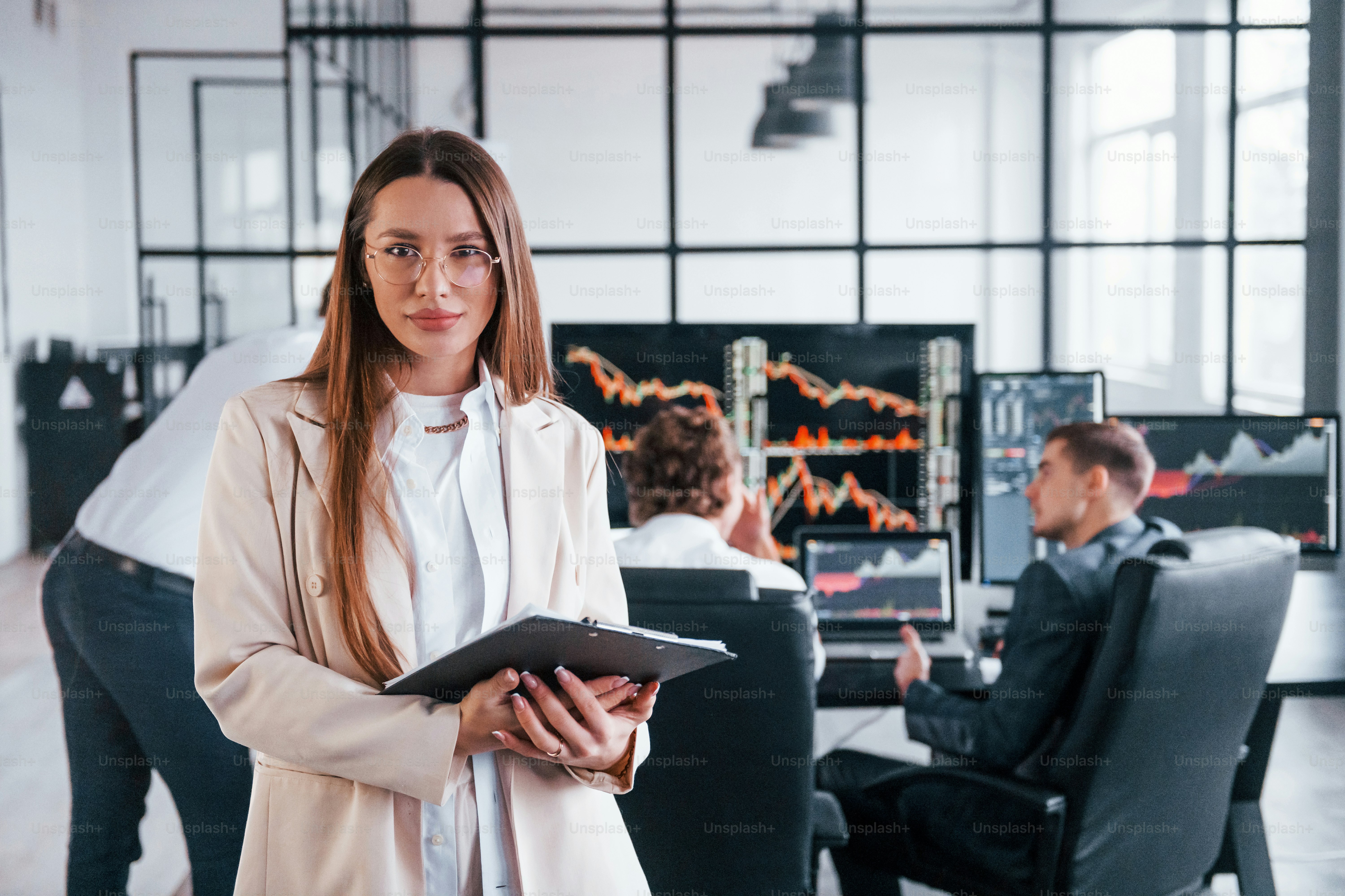 Female manager in front of colleguaes. Team of stockbrokers works in modern office with many display screens.