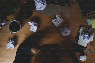 Overhead shot businessman sleeping on office desk surrounded by crumpled paper.