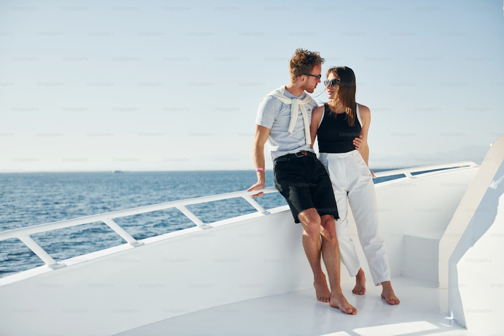 海に浮かぶヨットの上に立つ陽気な若いカップル。休暇の概念。