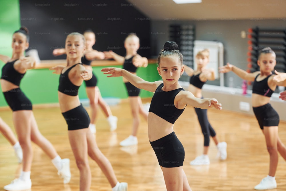 Stehen und synchronisierte Bewegungen. Gruppe weiblicher Kinder, die gemeinsam in Innenräumen sportliche Übungen machen.