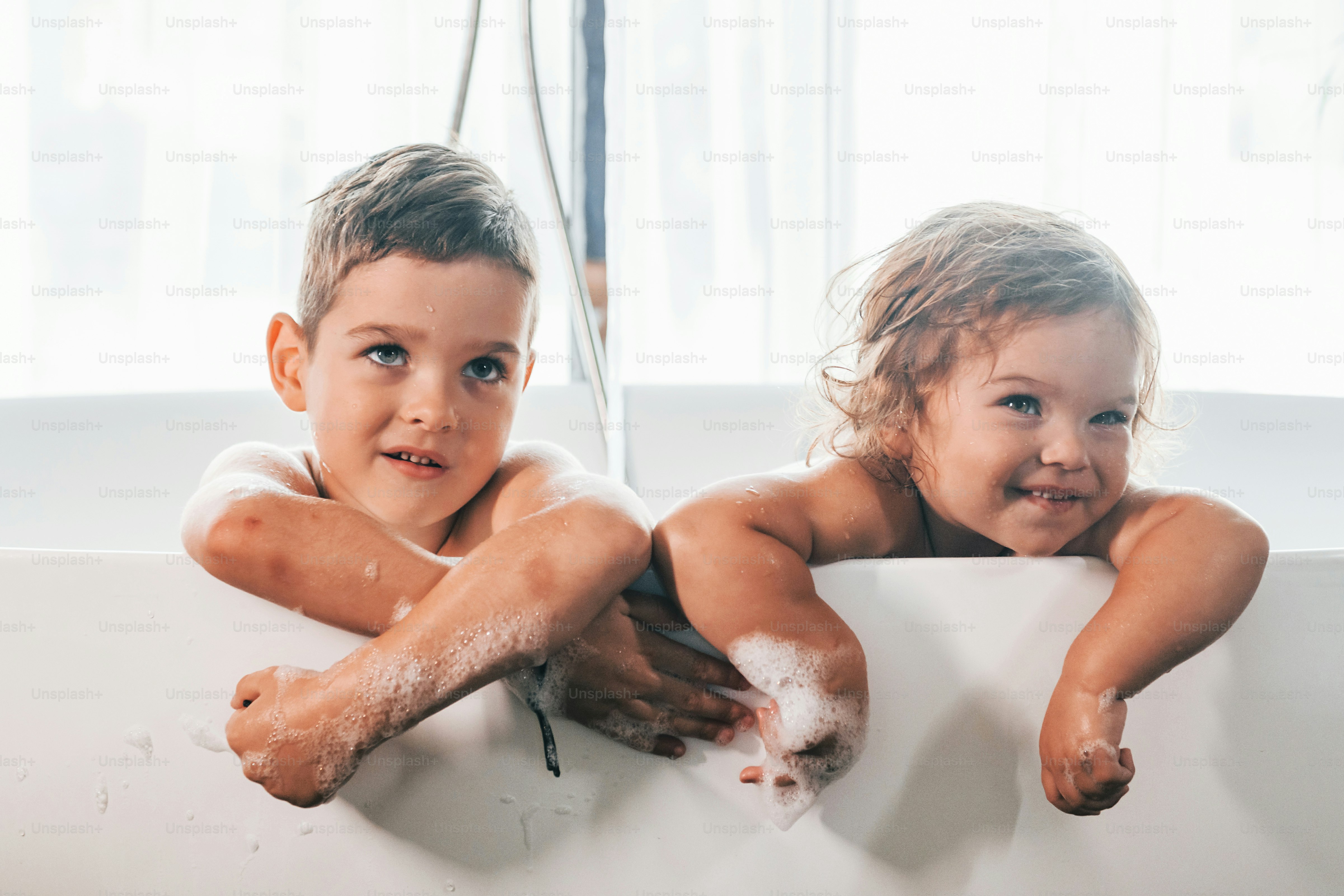 Two kids having fun and washing themselves in the bath at home. Posing ...