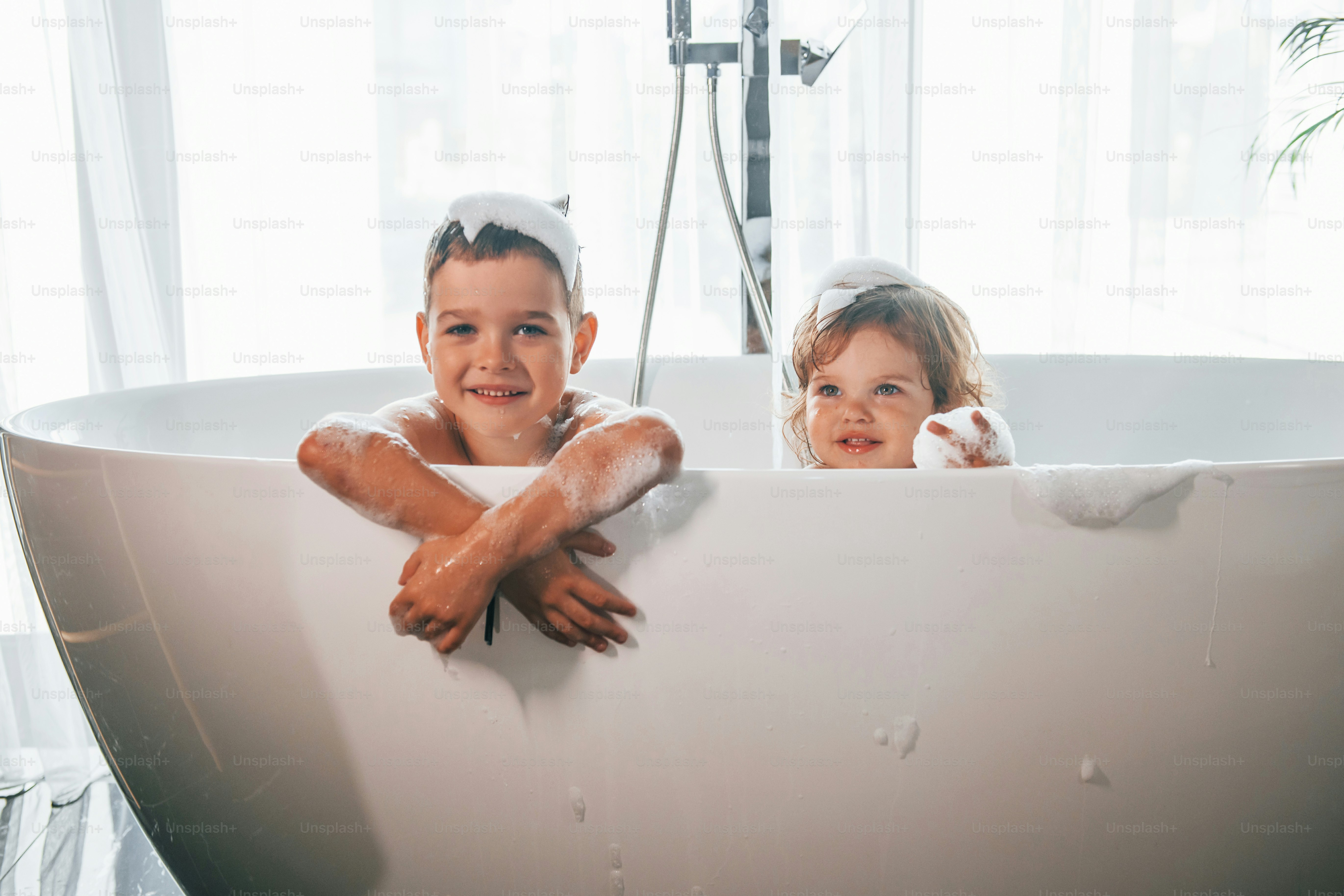 Two kids having fun and washing themselves in the bath at home. Posing ...