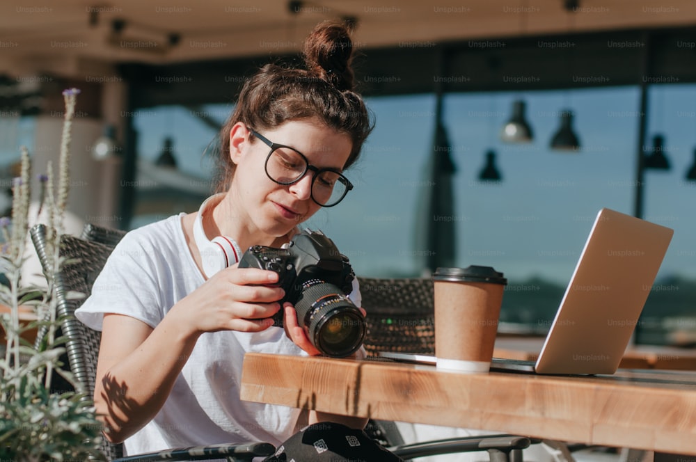 Photographe féminine regardant des photos sur l’appareil photo travaillant sur l’ordinateur portable à l’extérieur du café. Mise au point sélective.