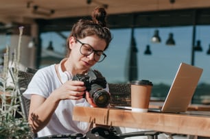 Female photographer watching photos on the camera working on the laptop in the cafe outdoor. Selective focus.