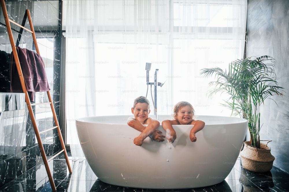Duas crianças se divertindo e se lavando no banho em casa. Posando para uma câmera.