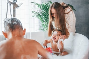 Having fun. Young mother helps her son and daughter. Two kids washing in the bath.