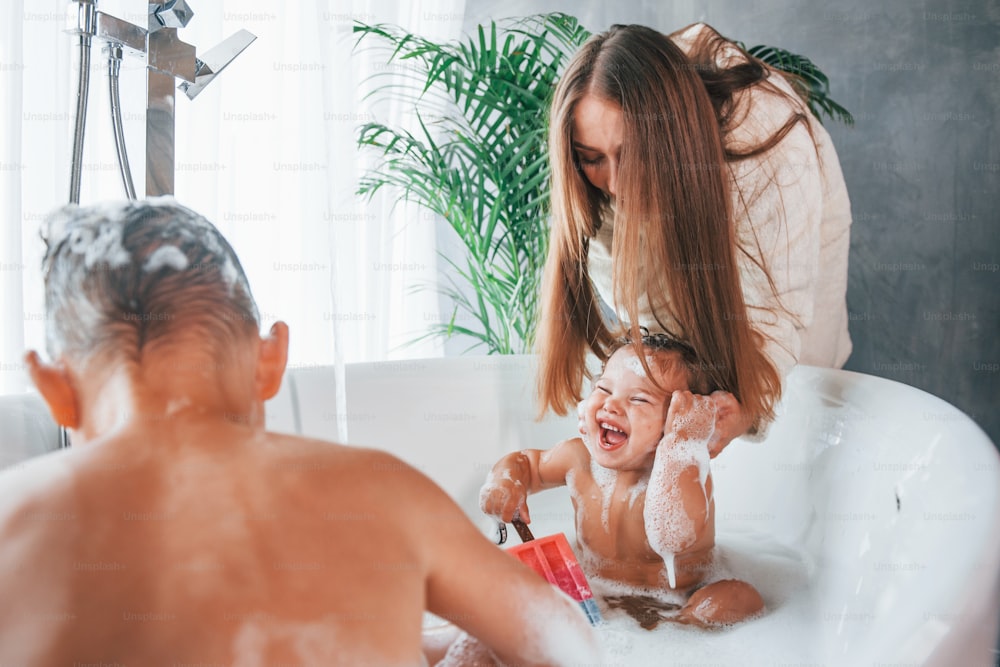 Having fun. Young mother helps her son and daughter. Two kids washing in the bath.