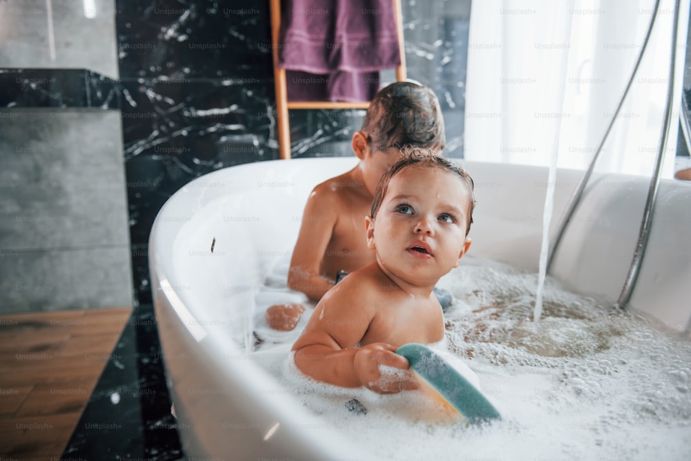 Due bambini che si divertono e si lavano nella vasca da bagno di casa. Aiutarsi l'un l'altro.