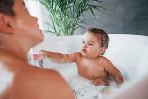 Two kids having fun and washing themselves in the bath at home.