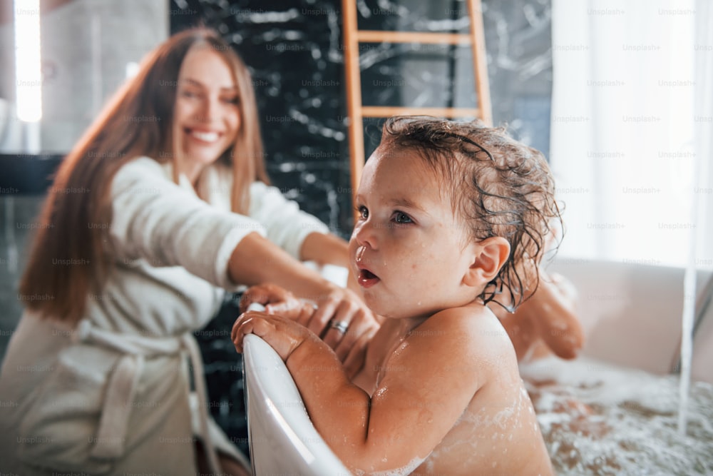 Die junge Mutter hilft ihrem Sohn und ihrer Tochter. Zwei Kinder waschen sich in der Badewanne.